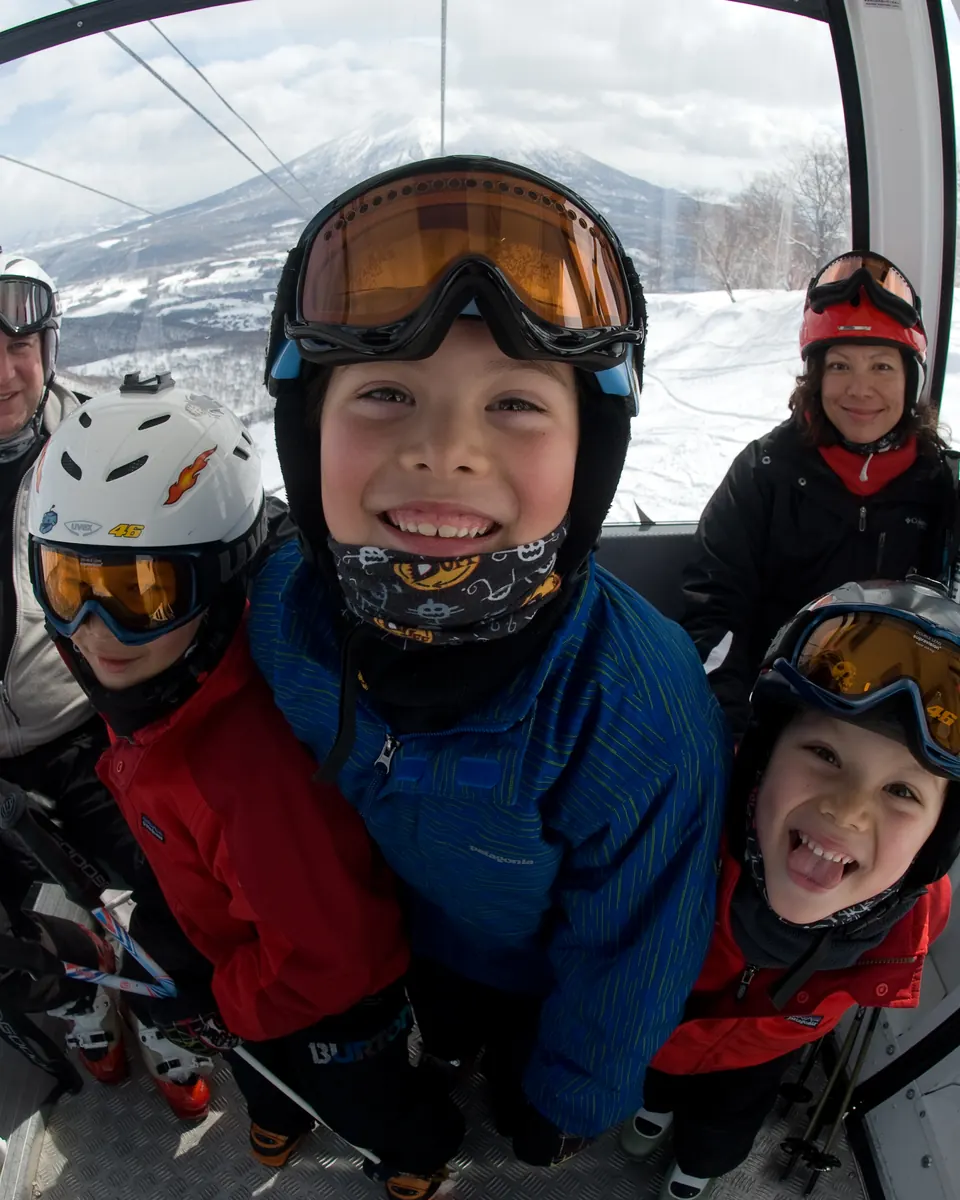 Family of five grinning in a Niseko gondola, Mt Yōtei through the window